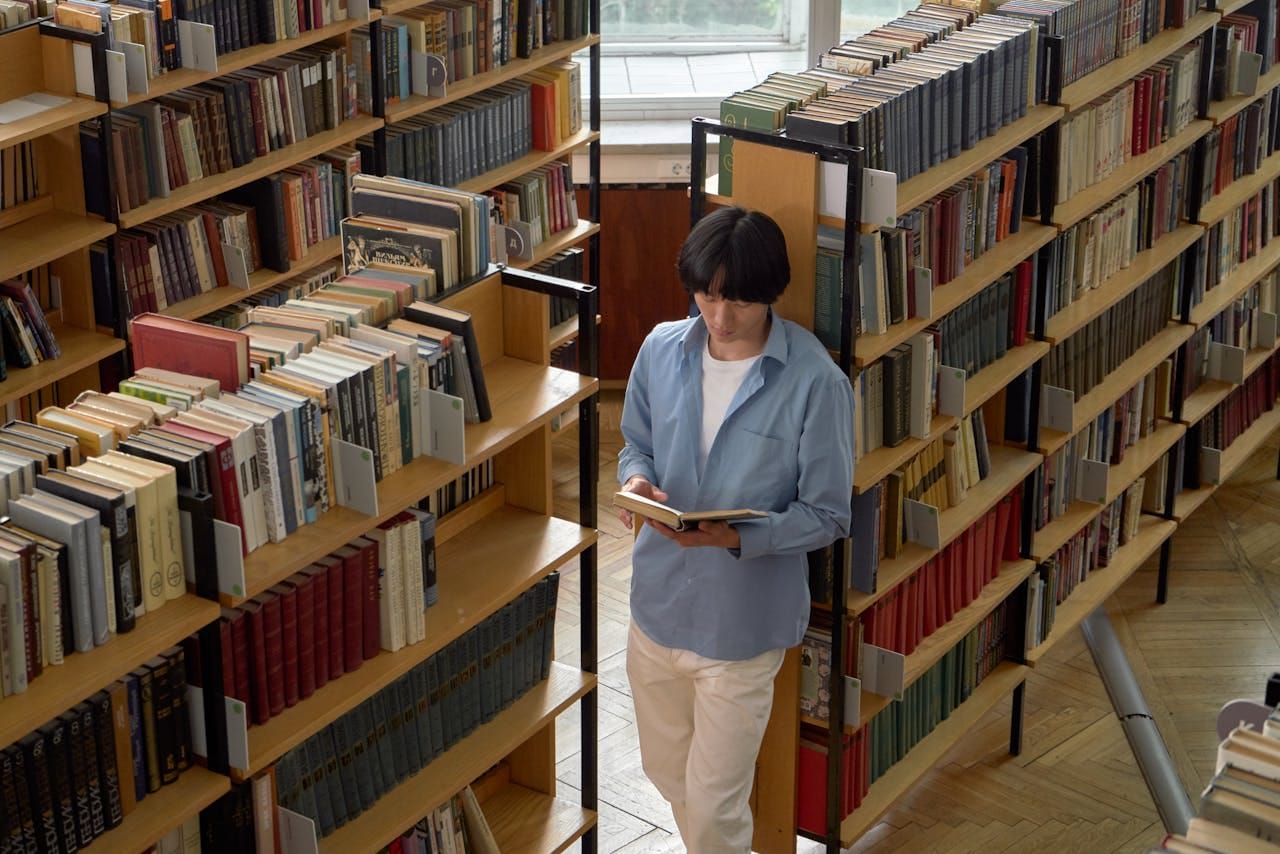 a-student-in-a-blue-long-sleeved-shirt-reading-a-book-in-a-library
