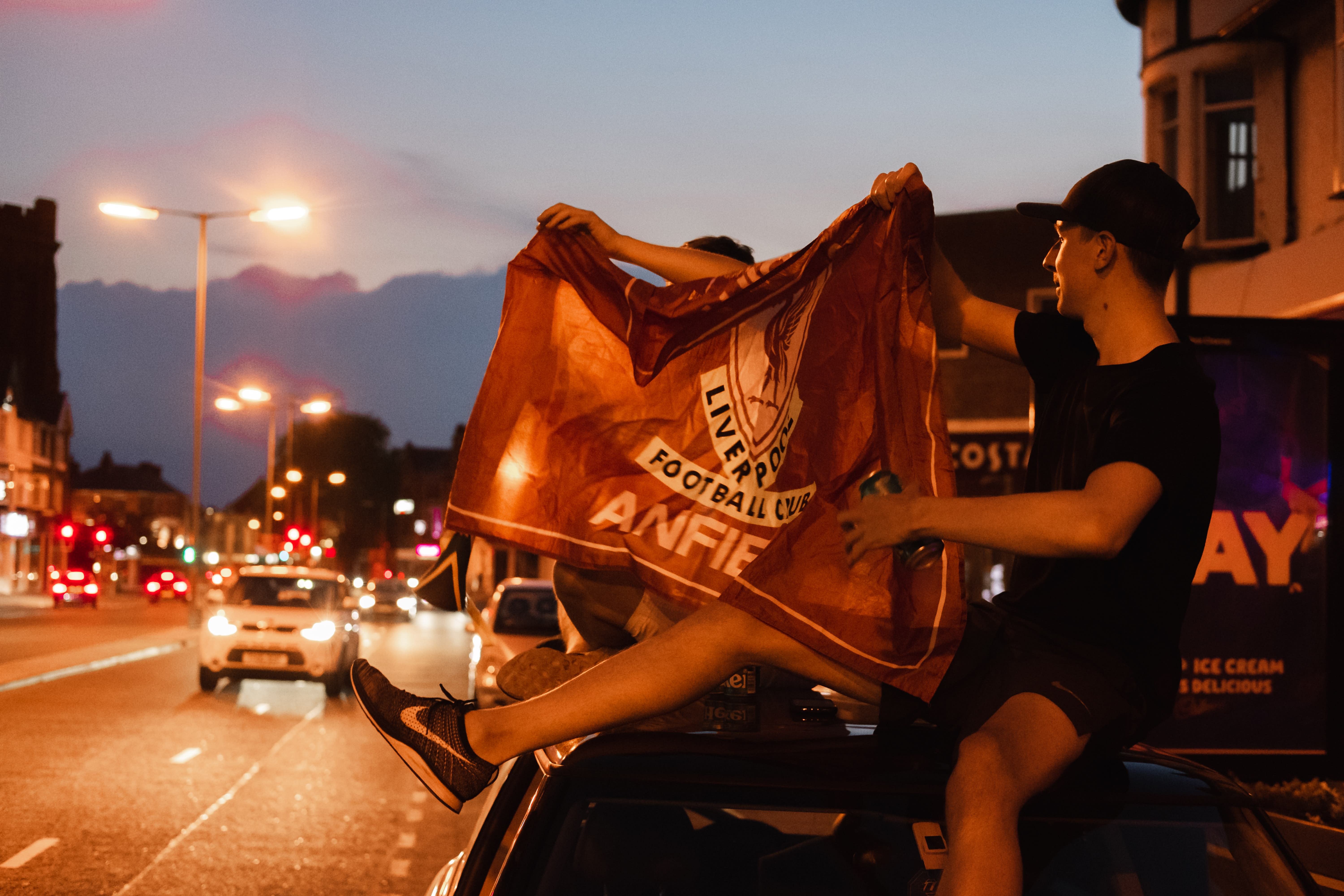 Fans holding a Liverpool flag atop a car 