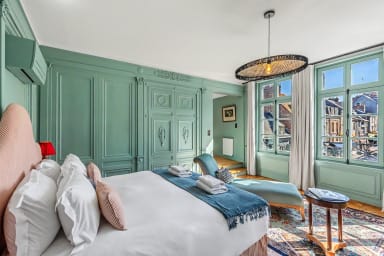 Chambre lumineuse avec fauteuil confortable et vue urbaine depuis la fenêtre.