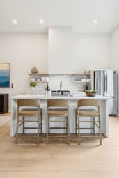 Modern kitchen with a white island, bar seating, and open shelving.