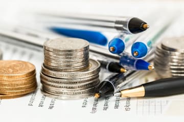 Stack of coins and pens placed on printed spreadsheets showing financial data