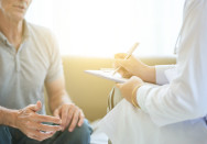 Ein Arzt im Gespräch mit einem männlichen Patienten, während der Arzt Notizen auf einem Klemmbrett macht. Das Bild symbolisiert ein vertrauliches Beratungsgespräch, möglicherweise zur Vasektomie oder einer medizinischen Untersuchung.