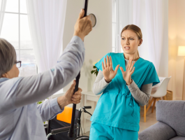 Eine wütende ältere Patientin erhebt ihren Stock und bedroht damit eine Krankenschwester in einem Pflegeheim. Eine angespannte Konfliktsituation, die emotionale Not, medizinische Herausforderungen und Schwierigkeiten bei der Pflege widerspiegelt.