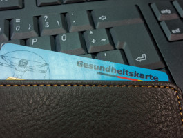 Elektronische Gesundheitskarte in einer Geldbörse vor einer Computertastatur als Symbol für die digitale Gesundheitsversorgung.