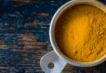 Eine Schale mit gelbem Kurkumapulver auf einem rustikalen Holztisch.