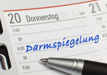 Ein Kalender mit einem Eintrag für Donnerstag, den 20., zeigt einen Termin um 8:00 Uhr mit der handschriftlichen Notiz "Darmspiegelung" in blauer Schrift. Ein Kugelschreiber liegt auf der rechten Seite des Eintrags.