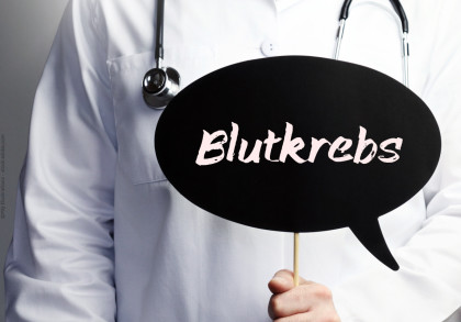 Ein Arzt in einem weißen Kittel hält ein Schild in Form einer Sprechblase. Auf dem Schild steht das Wort "Blutkrebs". Ein Stethoskop hängt um seinen Hals.