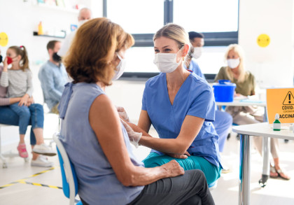 Eine Ärztin oder Krankenschwester in blauer medizinischer Kleidung und weißer Gesichtsmaske verabreicht einem ältere Patientin eine Impfung.