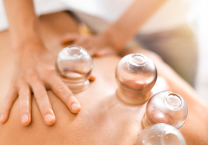 Nahaufnahme von Glas-Schröpfköpfen auf dem Rücken einer Person während einer Schröpftherapie. Eine Hand liegt auf dem Rücken der Person.