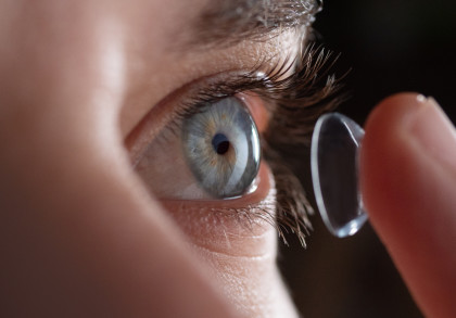 Nahaufnahme eines Auges mit blauer Iris, das dabei ist, eine Kontaktlinse aufzusetzen.