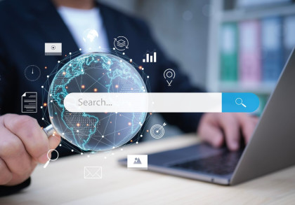 Ein Geschäftsman hält eine Lupe über einer symbolischen Weltkugel, die mit Netzwerklinien und Datenpunkten vernetzt ist. Ein Suchfeld mit der Aufschrift "Search..." und einer Lupe ist zentral platziert.