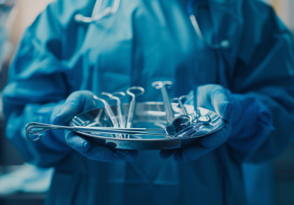 Nahaufnahme des Torsos eines Arztes, der eine Schale mit verschiedenen chirurgischen Instrumenten für eine Operation in beiden Händen hält.