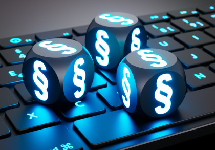 Auf einer schwarzen Tastatur liegen drei schwarze Würfel mit dem Paragraphen-Zeichen. Die Buchstaben der Tastatur leuchten neonblau.