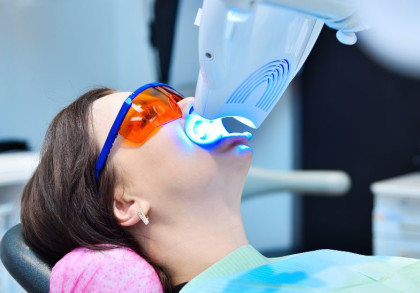 Eine Frau bleacht ihre Zähne, sie hält dafür ein kleines Bleachinggerät mit blauem Licht an ihren Mund.