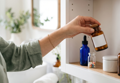 Pflegende Angehörige nimmt eine braune Medikamentenflasche aus einer gut sortierten Hausapotheke mit Tropfflaschen, Tabletten und weiteren Arzneimitteln.