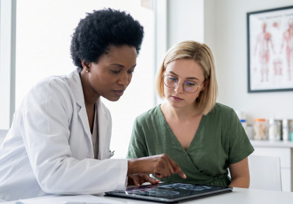 Ärztin bespricht mit einer Patientin medizinische Untersuchungsergebnisse auf einem Tablet.