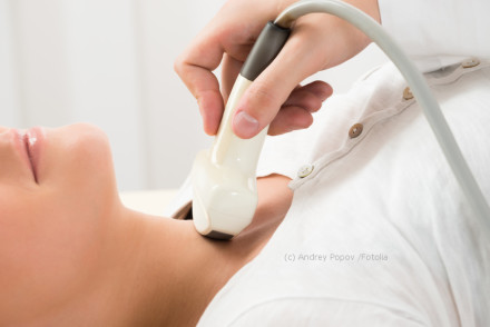 Nahaufnahme einer Person, die sich einer Ultraschalluntersuchung der Schilddrüse unterzieht. Eine Hand hält den Ultraschallkopf und bewegt ihn über den Hals der Person. Die Person liegt auf dem Rücken und trägt ein weißes Oberteil.