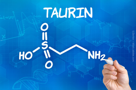 Chemische Strukturformel von Taurin auf einem blauen Hintergrund mit wissenschaftlichen Diagrammen und Molekülgrafiken. Das Wort "TAURIN" ist oben zu sehen. Eine Hand hält einen weißen Stift und deutet auf die chemische Formel.
