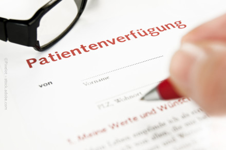 Nahaufnahme einer Hand, die dabei ist, mit einem Stift ein Dokument mit dem Titel "Patientenverfügung" auszufüllen. Eine Brille liegt neben dem Dokument.