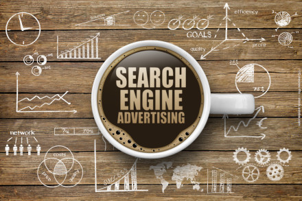 Eine Kaffeetasse auf einem Holztisch, gefüllt mit Kaffee, auf dem "Search Engine Advertising" steht. Um die Tasse herum sind Diagramme, Grafiken und Symbole mit Begriffen wie "Goals", "Quality" und "Efficiency" gezeichnet.