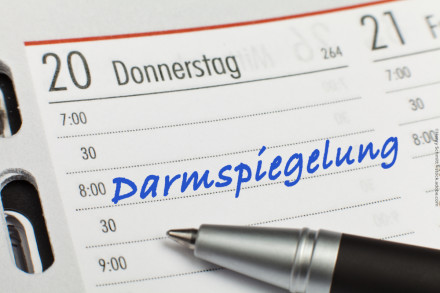 Ein Kalender mit einem Eintrag für Donnerstag, den 20., zeigt einen Termin um 8:00 Uhr mit der handschriftlichen Notiz "Darmspiegelung" in blauer Schrift. Ein Kugelschreiber liegt auf der rechten Seite des Eintrags.