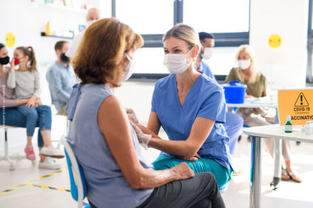 Eine Ärztin oder Krankenschwester in blauer medizinischer Kleidung und weißer Gesichtsmaske verabreicht einem ältere Patientin eine Impfung.