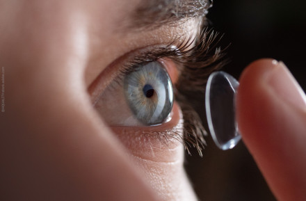 Nahaufnahme eines Auges mit blauer Iris, das dabei ist, eine Kontaktlinse aufzusetzen.