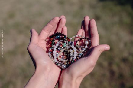Zwei Hände halten mehrere geflochtene Armbänder aus bunten Perlen und Edelsteinen, mit einem unscharfen Hintergrund aus Gras.