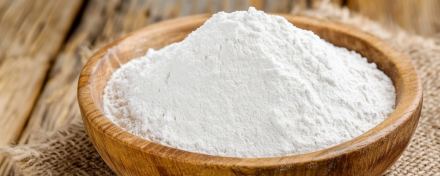 Holzschale mit feinem, weißem Proteinpulver auf Jutesack – Symbolbild für veganes Eiweiß aus pflanzlicher Quelle, z. B. Reis- oder Erbsenprotein in Pulverform.