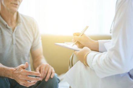 Ein Arzt im Gespräch mit einem männlichen Patienten, während der Arzt Notizen auf einem Klemmbrett macht. Das Bild symbolisiert ein vertrauliches Beratungsgespräch, möglicherweise zur Vasektomie oder einer medizinischen Untersuchung.