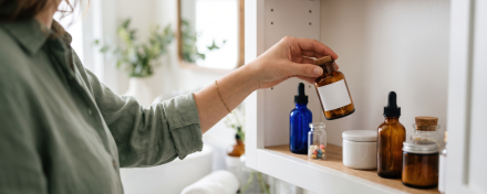 Pflegende Angehörige nimmt eine braune Medikamentenflasche aus einer gut sortierten Hausapotheke mit Tropfflaschen, Tabletten und weiteren Arzneimitteln.