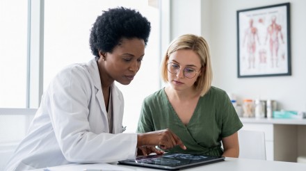 Ärztin bespricht mit einer Patientin medizinische Untersuchungsergebnisse auf einem Tablet.
