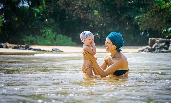 Junge Mutter in einem Flusslauf hält Ihr Baby lächelnd hoch