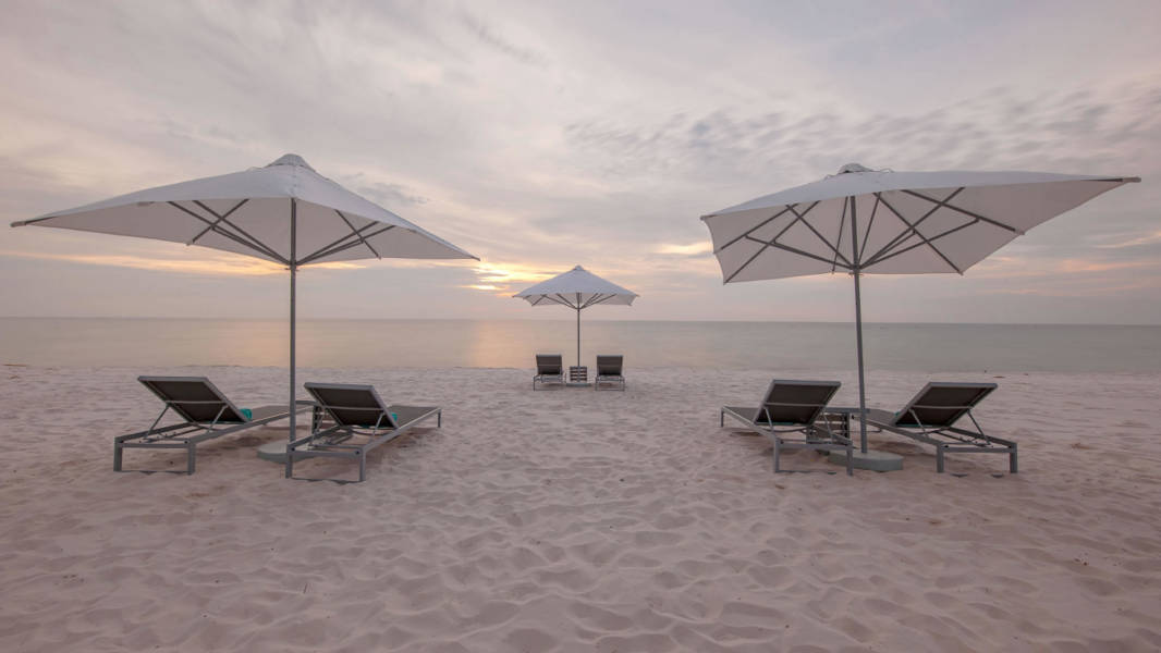 a couple of lawn chairs sitting on top of a sandy beach