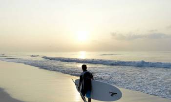 a man in a wet suit standing on a beach holding a surf board
