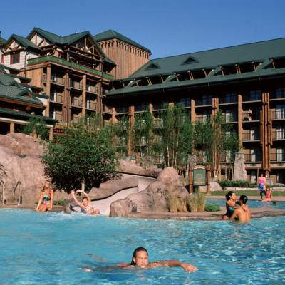 a group of people swimming in a pool of water with Disney's Wilderness Lodge in the background