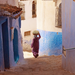 Frau im Gewand trägt etwas auf ihrem Kopf die Treppen in Chefchaouen, Marokko, hinunter