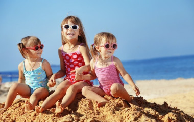 Drei kleine Mädchen mit Sonnenbrillen lachen am Sandstrand