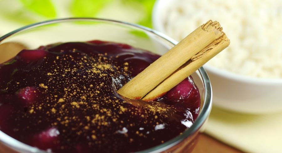 A traditional Peruvian dessert called mazamorra morada made out of purple corn and seasoned with cinnamon with rice pudding in the background (Selective Focus, Focus on the cinnamon stick)
