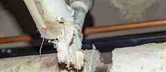 Close-up of a broken pipe covered in insulation material, with rough, jagged edges and exposed metal. The damaged area reveals fraying insulation and possible signs of water or age-related deterioration.