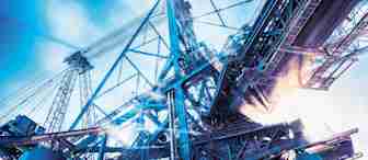 A towering industrial structure with cranes and metal beams is shown against a bright blue sky. The scene depicts a construction or manufacturing facility, with beams of light creating an energized atmosphere. Cloudy elements and sun rays filter through the industrial setting.