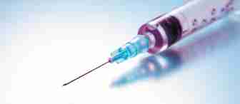 A close-up shot of a syringe with a sharp needle, filled with a red liquid, placed against a smooth gradient background of light blue and white. The syringe is slightly angled, with the needle pointing to the left.