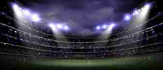 A dimly lit, large football stadium at night with bright floodlights illuminating the field. The stands are filled with spectators, and the atmosphere is vibrant. Confetti can be seen falling, creating a celebratory scene, while the green pitch is ready for action.