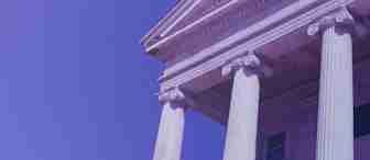 A classic building with tall Ionic columns and a triangular pediment is shown from a low angle against a clear blue sky, highlighting the architectural details. The photograph has a purple tint cast over it.