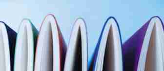 Close-up view of several colorful open notebooks standing upright side-by-side, with their pages and covers facing outward. The background is a soft blue, which contrasts with the vibrant colors of the notebook covers, creating a visually appealing composition.