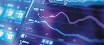 Close-up of a digital trading screen displaying multiple financial charts and graphs. The screen shows real-time market data, including line and candlestick charts, various indicators, and numerical values. The background has a blue and purple color scheme with a blurred effect.