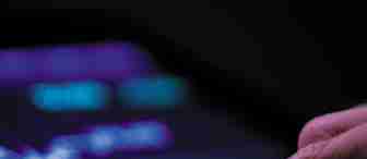 A person taps a tablet screen displaying a digital stock trading interface with various graphs, charts, and numbers lit up in neon purple and blue against a dark background. The prominent graph shows upward and downward trends.