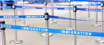 A zigzag queue setup with blue stanchions and barriers labeled "IMMIGRATION" in white text, typically found at an airport or border control area. The image shows an empty queuing space with multiple lines and posts.