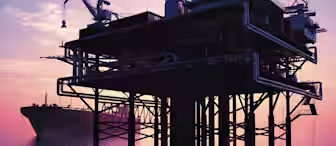 Silhouetted offshore oil platform in calm water during sunset, with a large ship anchored in the background. The sky is painted in hues of purple, pink, and orange, creating a serene and reflective atmosphere.