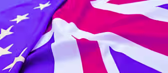 A close-up of the American and UK flags arranged side by side, creating a waving pattern. The stars from the American flag and the red, white, and blue design of the UK flag are prominently visible and blend together in the center.